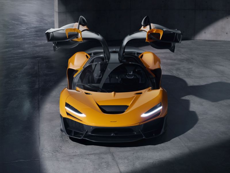 McLaren W1 2025 orange, face avant avec portes papillon ouvertes, design spectaculaire et signature lumineuse LED