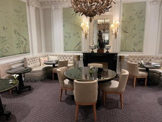 Intérieur du salon du San Régis avec banquettes claires, tables rondes et panneaux décoratifs botanistes