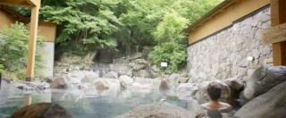 Onsen en plein air au Japon entouré de végétation luxuriante, avec des visiteurs se relaxant dans un bassin rocheux