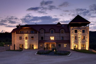 Façade en pierre du Domaine de la Klauss illuminée sous un ciel de crépuscule violet.