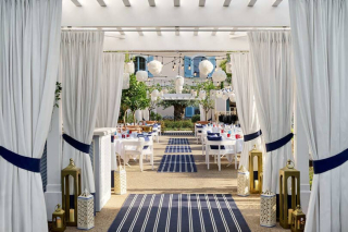 Espace de restauration extérieur The Strand avec tapis rayés et pergolas.