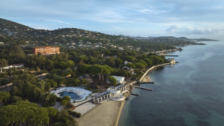 Vue aérienne de l'hôtel COMO Le Beauvallon et de la côte, montrant le bâtiment ocre de style Belle Époque, le beach club et le golfe de Saint-Tropez.