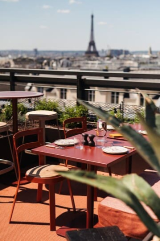 Tables et chaises rouges sur la terrasse du rooftop Fuga R. à Paris, avec une vue dégagée sur la tour Eiffel et les toits parisiens en arrière-plan.