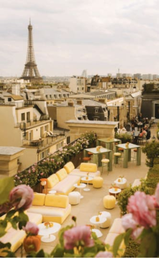 Le toit-terrasse de l'hôtel Peninsula Paris, aménagé avec des canapés jaunes et roses, des tables vertes et de belles roses au premier plan, avec la Tour Eiffel en arrière-plan.