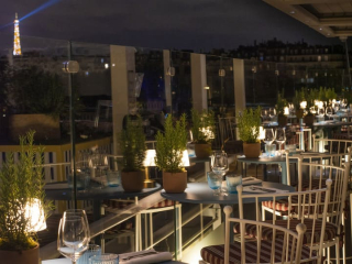 Le rooftop de l'Hôtel Molitor la nuit. Un bar rayé portant l'inscription MOLITOR, des espaces lounge éclairés par de petites lampes de table, surplombant la célèbre piscine extérieure illuminée en bleu.